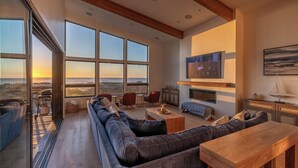 A spacious living room with a large sofa, a wooden coffee table, and a TV mounted on the wall.