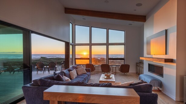 A modern living room with a large window overlooking the ocean, a sofa, a coffee table, and a flat-screen TV mounted on the wall.