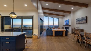 A modern kitchen with a large island, wooden flooring, and a view of the ocean.