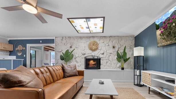 A living room with a leather sofa, a fireplace, a ceiling fan, and a stone wall.