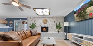 Un salon avec un canapé en cuir, une cheminée, un ventilateur de plafond et un mur en pierre.