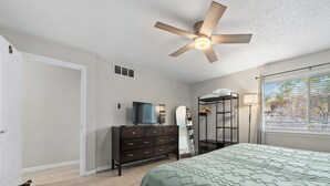 A bedroom with a bed, dresser, TV, mirror, and a ceiling fan.