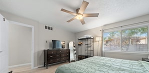 A bedroom with a bed, dresser, TV, mirror, and a ceiling fan.