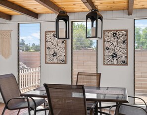 A covered patio with a table and chairs, framed floral artwork on the walls, and a wooden ceiling.