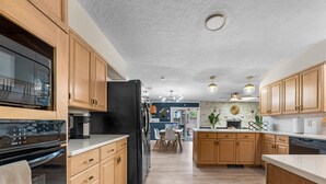 A modern kitchen with wooden cabinets, a black refrigerator, a coffee maker, and a dining area with a table and chairs.