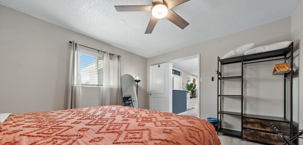 Une chambre à coucher comprenant un lit, un ventilateur de plafond, une armoire et une porte donnant sur une autre pièce.