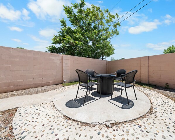 An outdoor patio with a round table and four chairs, surrounded by a low brick wall and a tree.