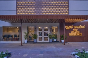 The entrance of Grand Continental with a modern design, featuring a wooden canopy and potted plants.