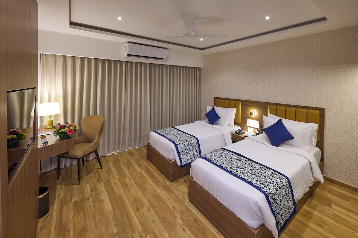 Quarto de hotel com duas camas, uma escrivaninha com cadeira, televisão e ar condicionado.