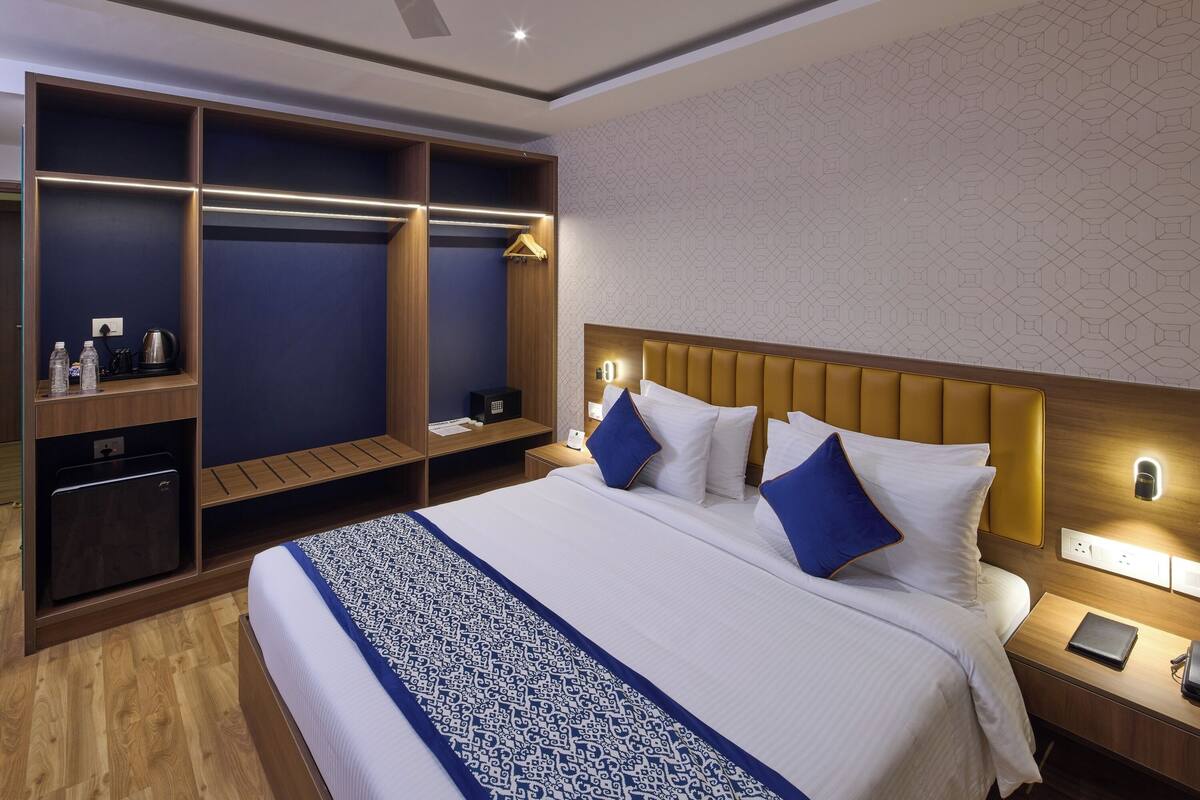 Quarto de hotel com cama grande, guarda-roupa com espelho, mesa de cabeceira com abajur e luminária na parede.