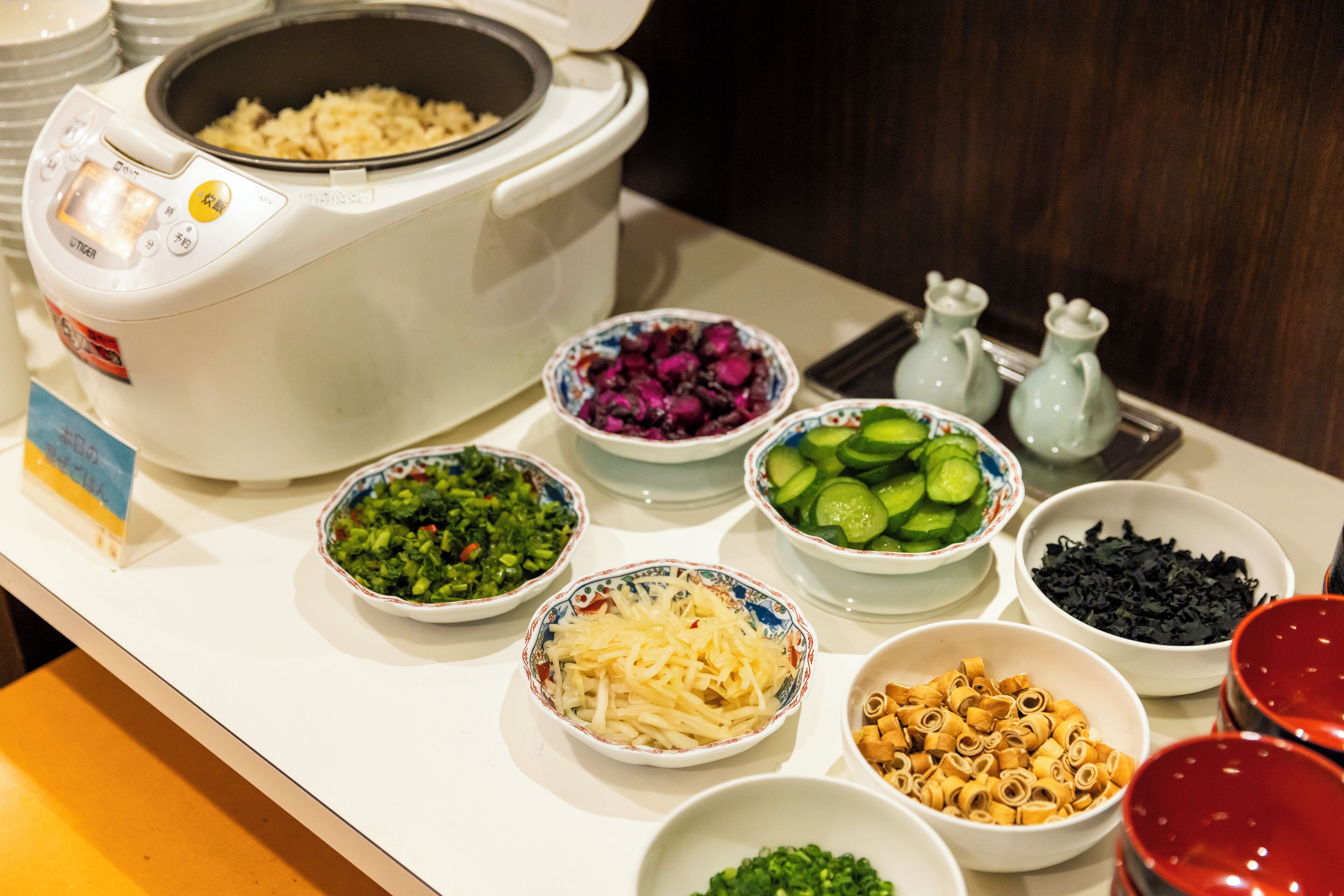 A kitchen counter with a rice cooker, bowls of various ingredients, and condiments.