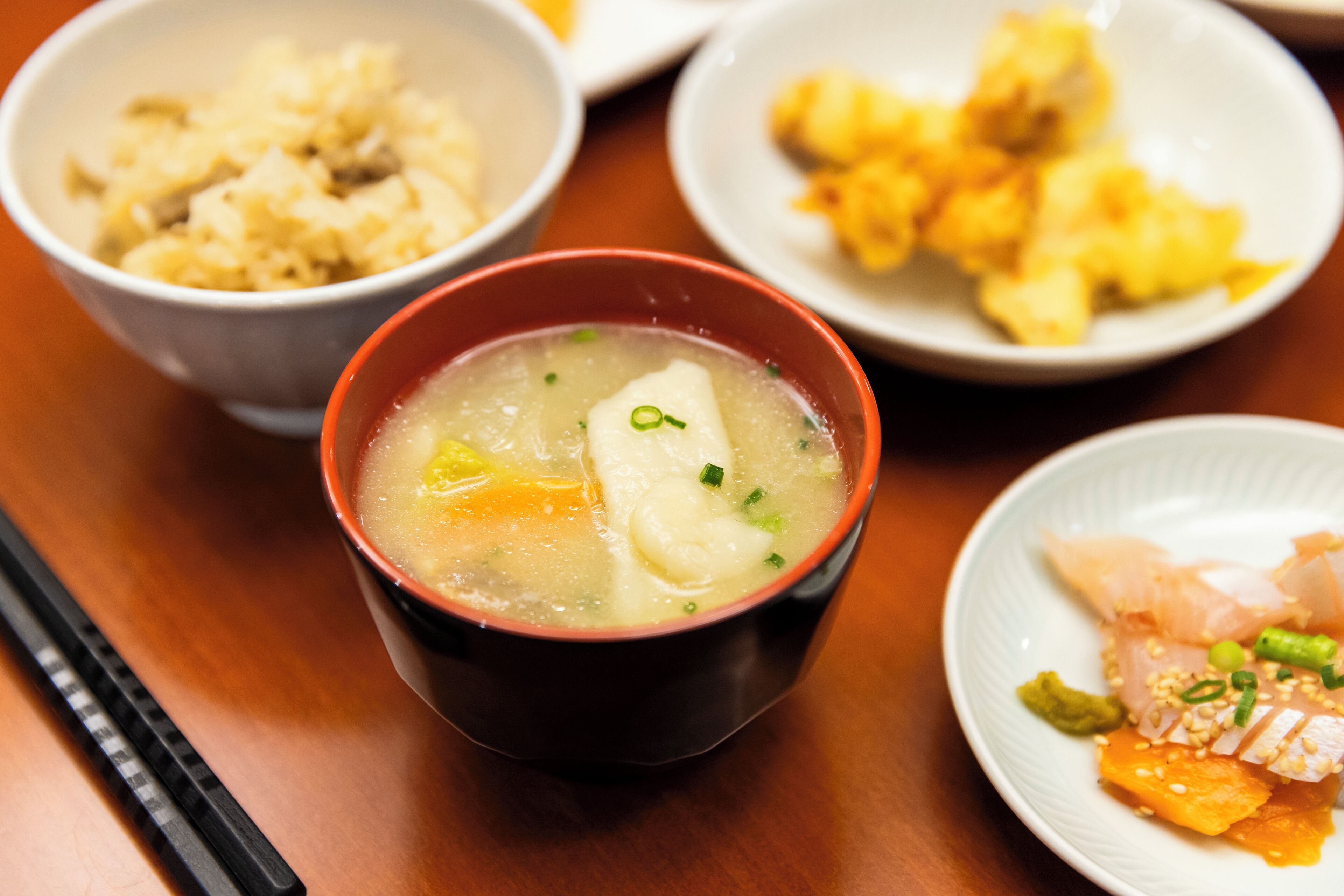 Una mesa con tazones de comida, incluyendo sopa de tofu y cebolletas, y otros platos.