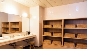 Une salle de bain avec un grand miroir, un lavabo, deux tabourets et des étagères avec des paniers en osier.