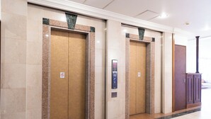 Un couloir avec trois portes d’ascenseur, chacune équipée d’un panneau de commande et d’un panneau indiquant qu’il est interdit de fumer.