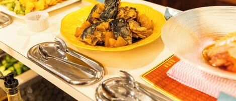 Una mesa de bufé con diversos platos, entre ellos mariscos y verduras, además de utensilios para servir.