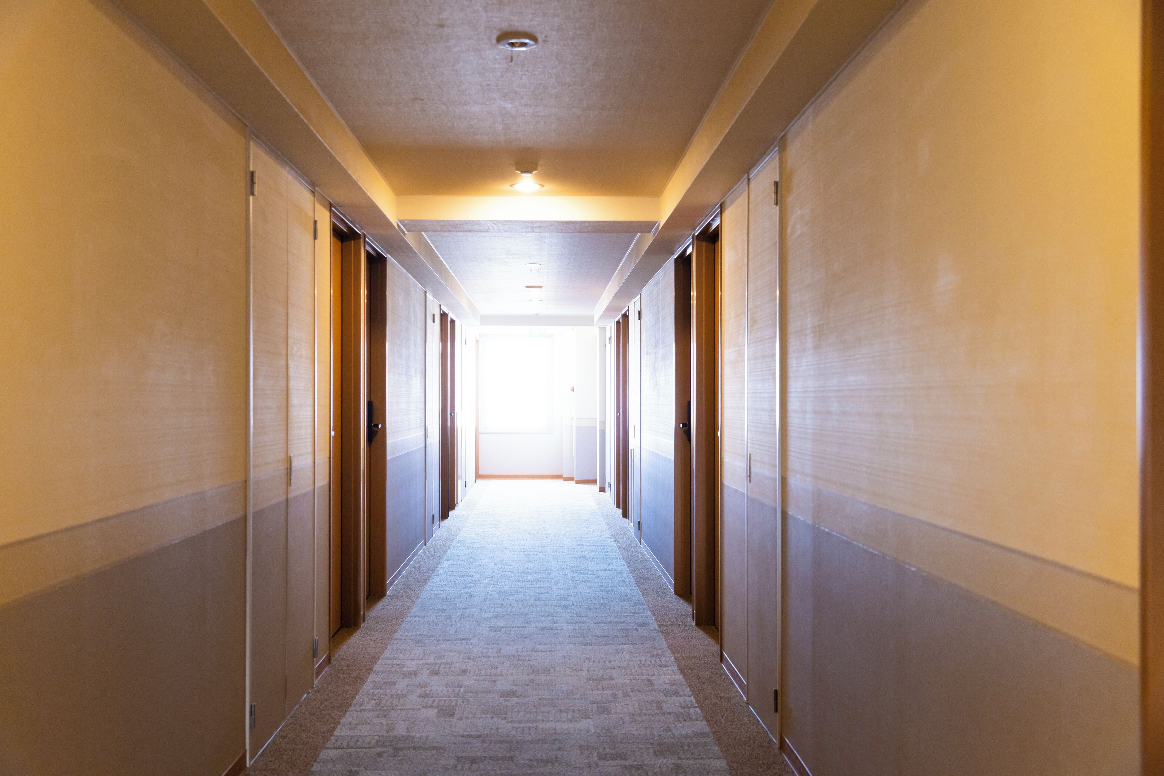A long, narrow hotel corridor with doors on both sides leading to rooms.
