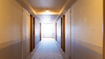 A long, narrow hotel corridor with doors on both sides leading to rooms.