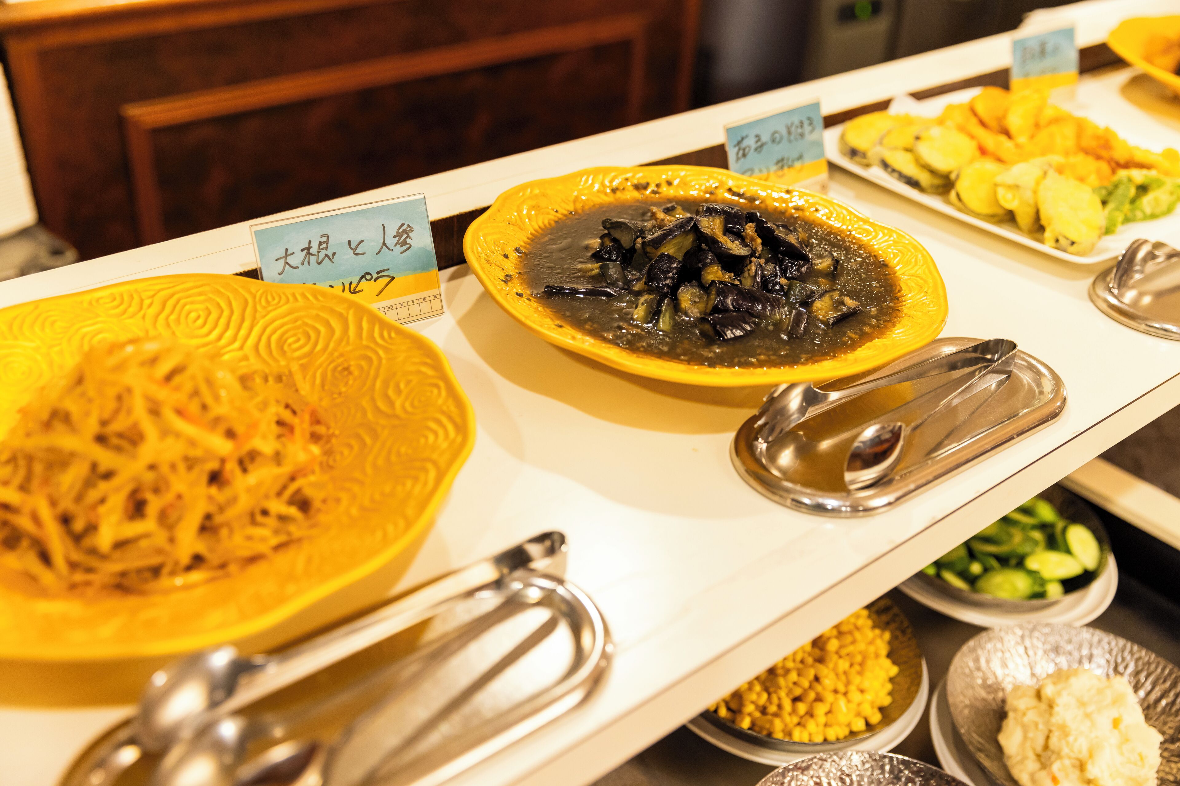 A buffet with various dishes including a yellow plate with shredded food, a black sauce dish, and a plate of sliced vegetables.