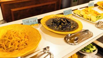 A buffet with various dishes including a yellow plate with shredded food, a black sauce dish, and a plate of sliced vegetables.