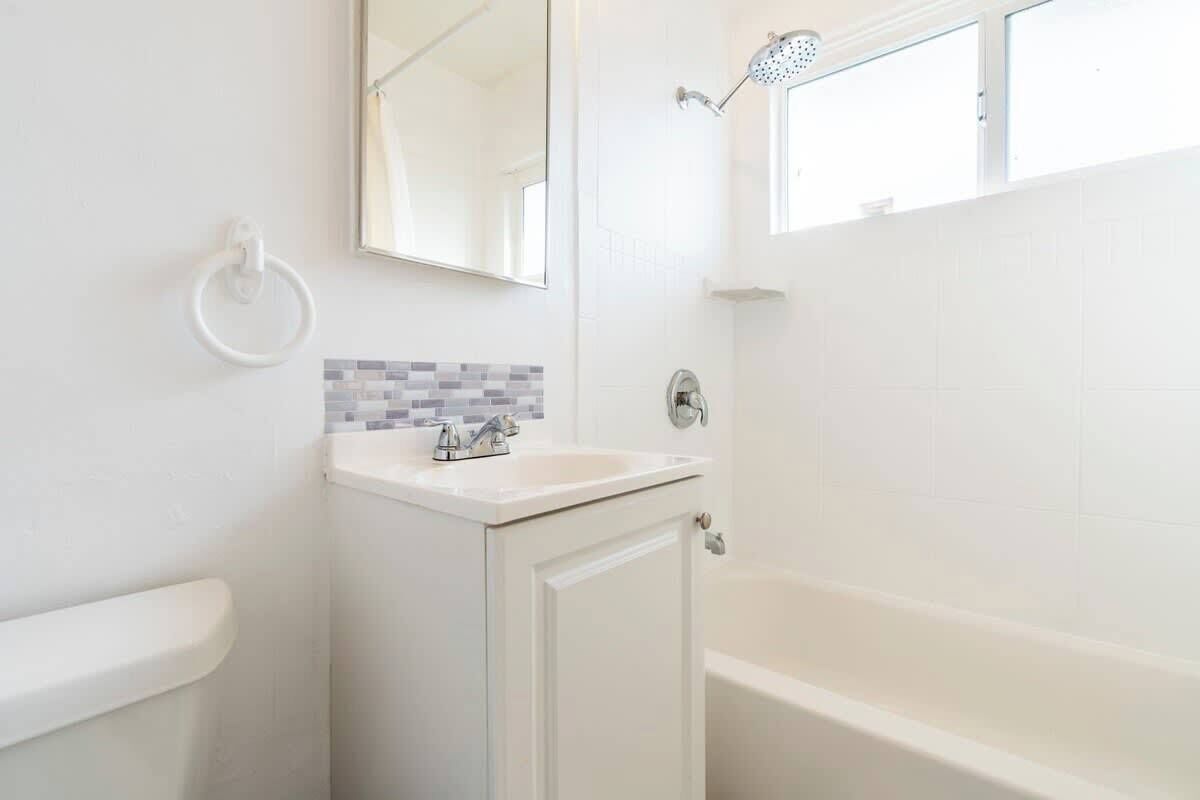 A bathroom with a white sink, a mirror, a shower, and a tiled wall.