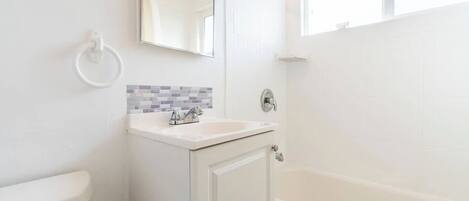 A bathroom with a white sink, a mirror, a shower, and a tiled wall.