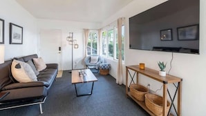 Una sala de estar moderna con un sofá, una mesa de centro, un televisor y un ventanal con cortinas.