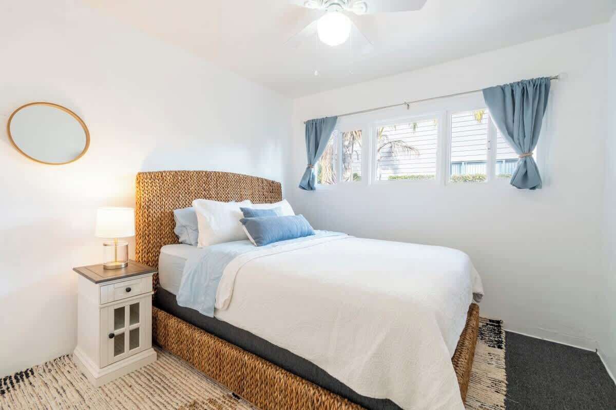 A bedroom with a bed, a nightstand, a lamp, a window with curtains, and a ceiling fan.