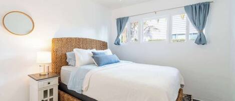 A bedroom with a bed, a nightstand, a lamp, a window with curtains, and a ceiling fan.