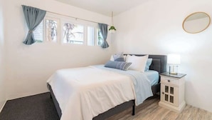 Une chambre à coucher avec un lit, une table de chevet, un miroir et une fenêtre avec des rideaux.