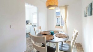 Un coin repas comprenant une table ronde, quatre chaises, des sets de table en fibres tressées et un luminaire suspendu.