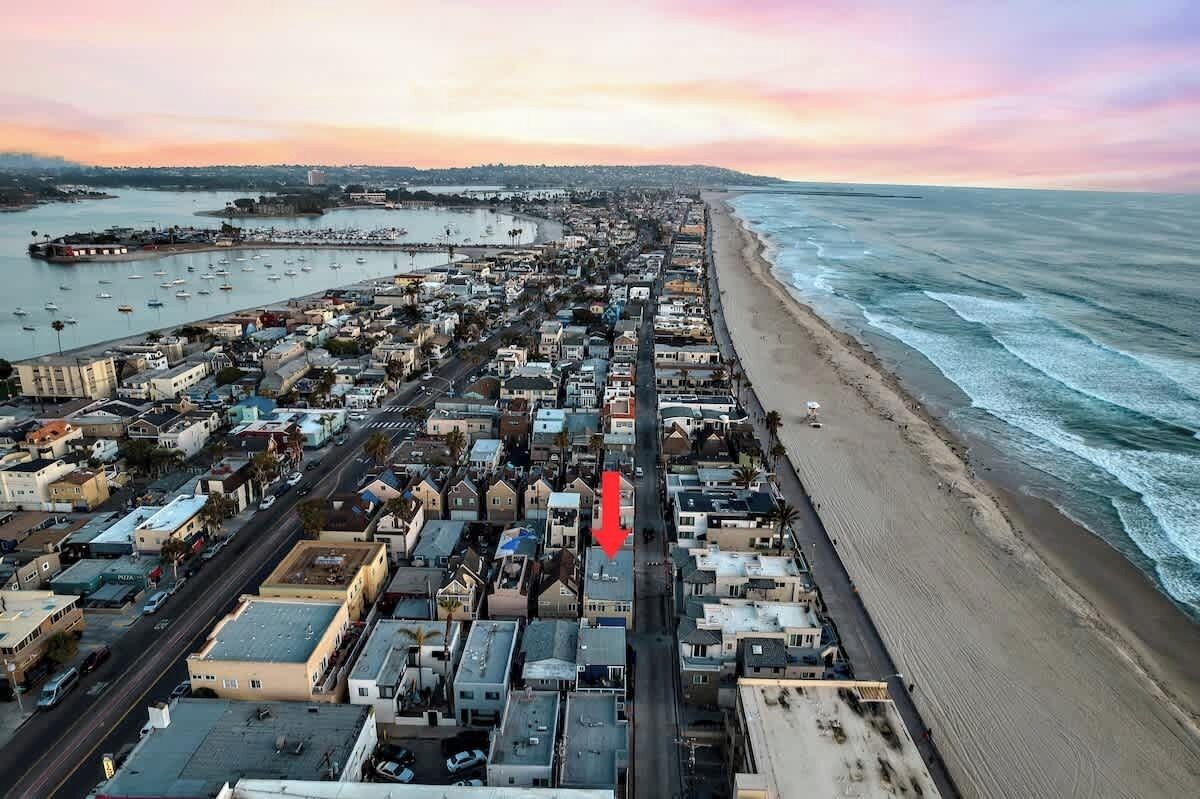 Vista aerea di una cittadina costiera con spiaggia, porto turistico e fitta edilizia lungo il lungomare.