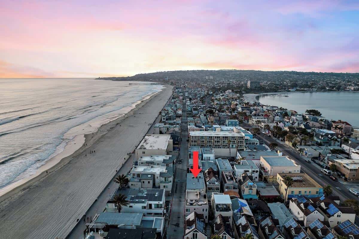 An aerial view of a coastal town with a beach, buildings, and a pier.