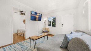 A modern, well-lit room with a large bed, a small table, a chair, and a TV mounted on the wall.