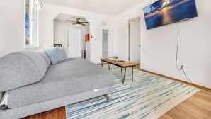A modern living room with a grey sofa, a wooden coffee table, and a large TV mounted on the wall.