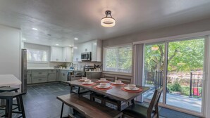 A modern kitchen with a dining area, featuring a large table with chairs, a built-in microwave, and a view of the outdoors through large windows. - Hot Tub Family Home with Mountain Views - Close to Red Rocks and Clear Creek! (Golden)