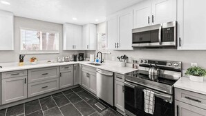 A modern kitchen with white cabinets, a stainless steel stove, and a microwave. - Hot Tub Family Home with Mountain Views - Close to Red Rocks and Clear Creek! (Golden)