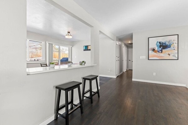 A spacious kitchen with a white countertop, two black barstools, and a window with blinds.