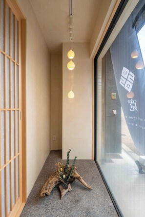 A hallway with a wooden shoji screen, a decorative plant, and hanging pendant lights. - KUTSUROGI SAUNA and STAY (Tokyo)