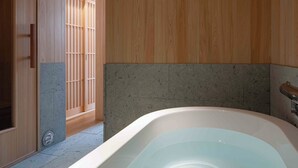 A modern bathroom with a freestanding bathtub, wooden panel walls, and a stone accent wall. - KUTSUROGI SAUNA and STAY (Tokyo)