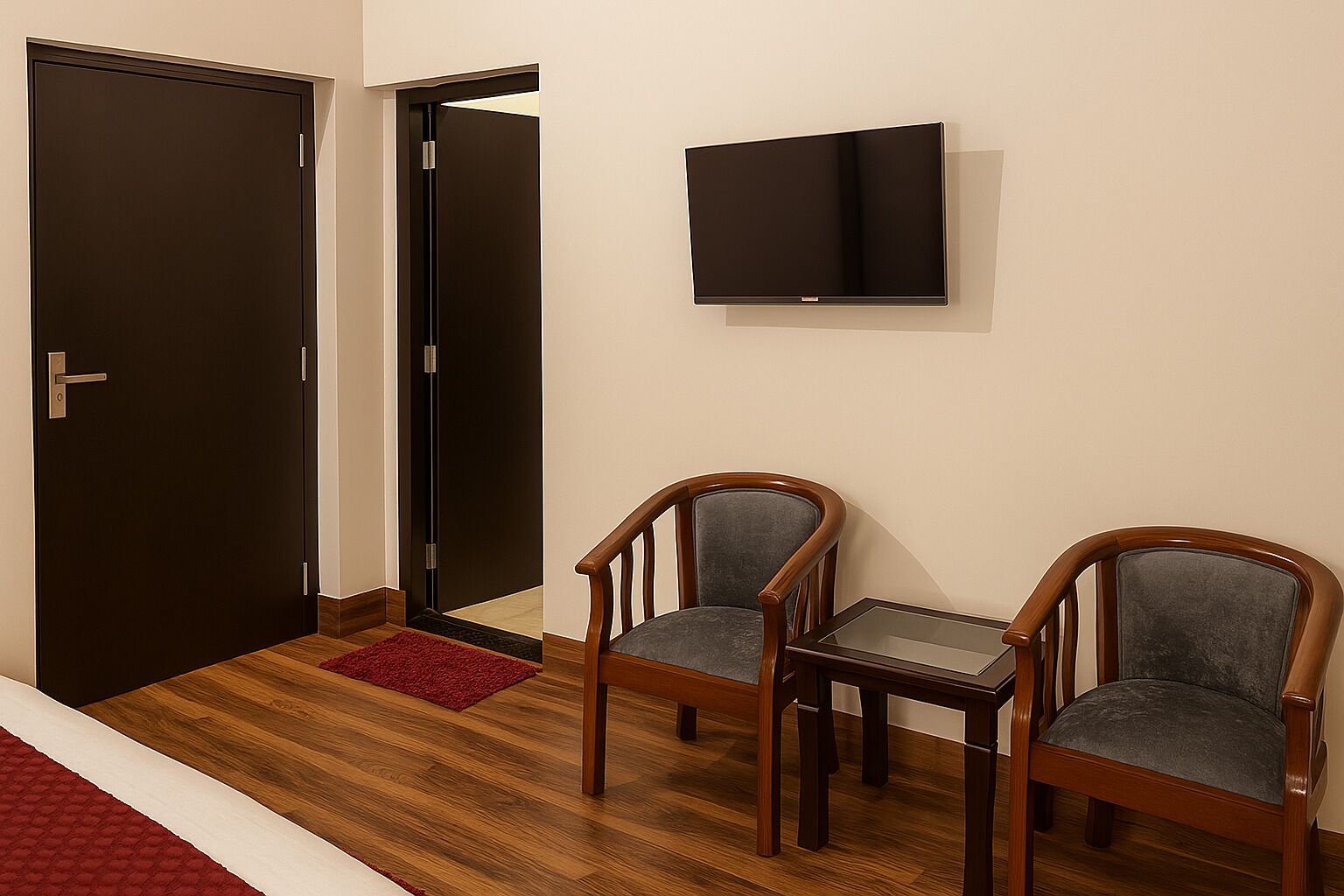 A room with a closed door, a television mounted on the wall, and two wooden chairs with grey cushions.