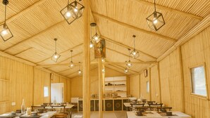 A spacious room with wooden walls and ceiling, multiple tables and chairs, and hanging pendant lights.
