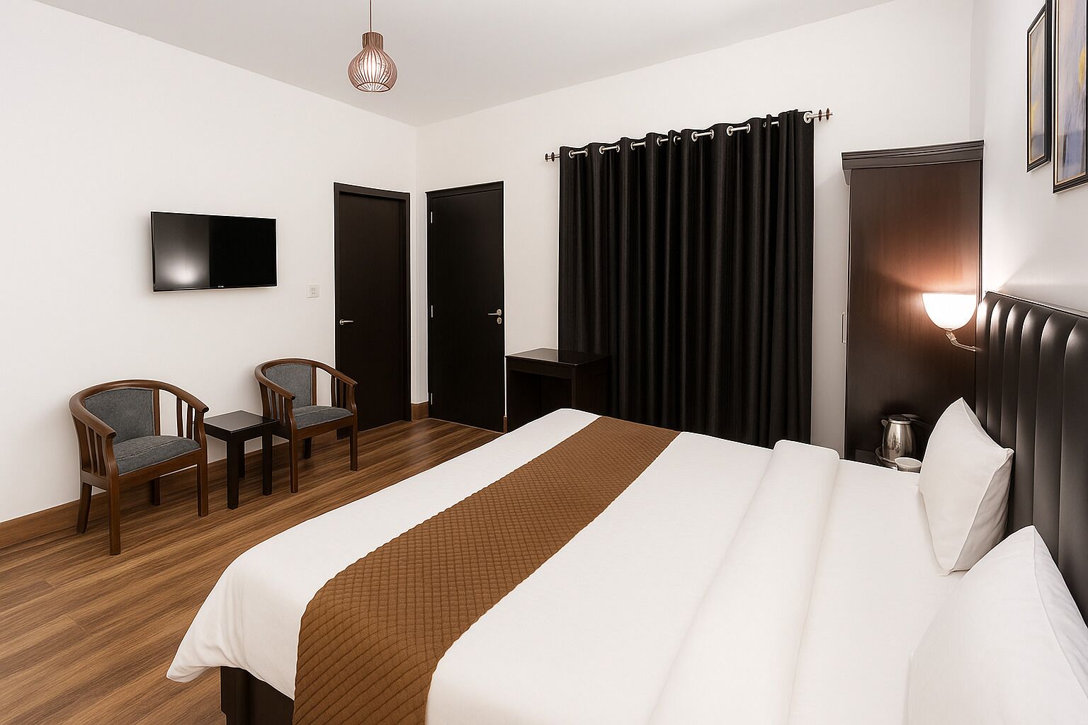 A hotel room with a bed, two chairs, a TV, a desk, a curtain, and a wall-mounted light.