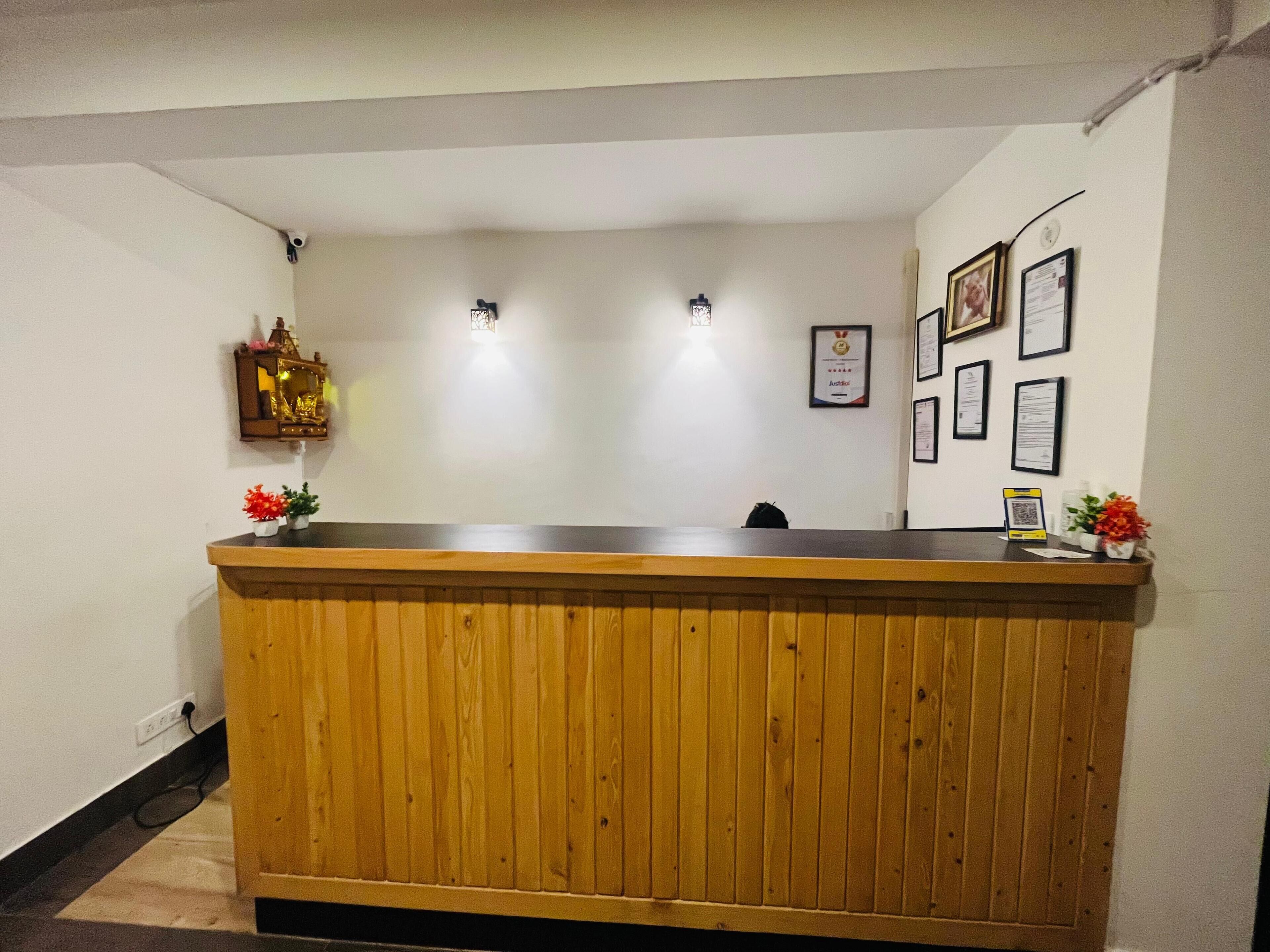 A reception desk with a wooden finish, a small shrine with a statue, and framed certificates on the wall.