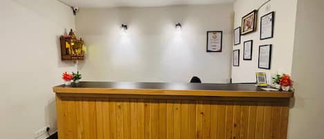 Una recepción con detalles de madera, un pequeño santuario con una estatua y certificados enmarcados en la pared.
