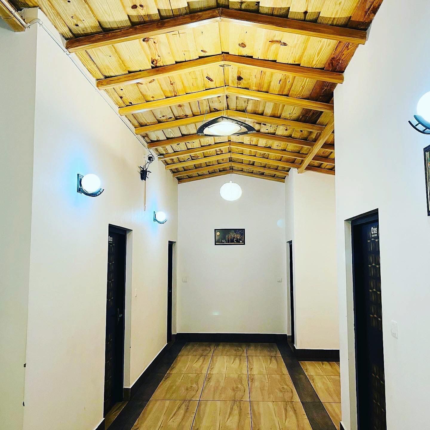 Un couloir avec des poutres en bois au plafond, des murs blancs et des portes noires.