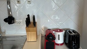 Una cucina con lavello, tagliere in legno, porta coltelli, macchina da caffè rossa e nera e tostapane nero.