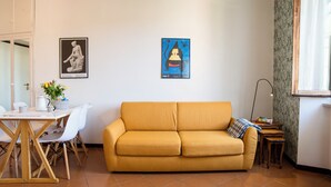Un soggiorno con un divano giallo, un tavolo da pranzo con sedie, un tavolino e due opere d'arte incorniciate appese al muro.