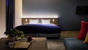 Una habitación de hotel con cama, mesita de noche y un pequeño sofá.