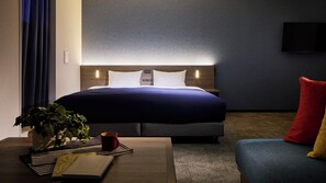 Een hotelkamer met een bed, nachtkastje en een kleine bank.