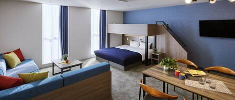 Una habitación de hotel moderna con una cama litera, un sofá, una mesa de comedor con sillas y un televisor montado en la pared.